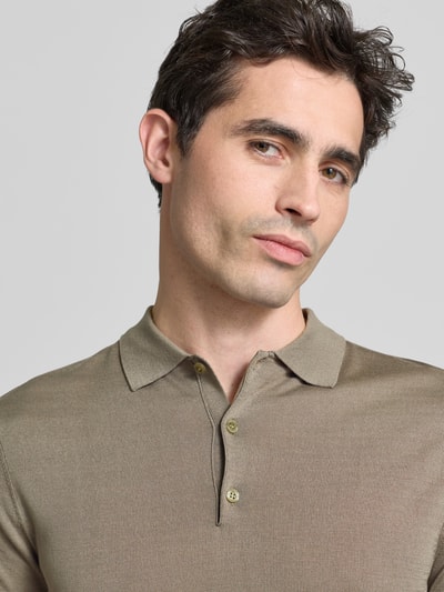 Mężczyzna nosi Slim Fit Poloshirt aus Lyocell-Seide-Mix von GUESS, model 'LARRY', kołnierzyk polo, listwa guzikowa, paski w kontrastowym kolorze, długość tyłu w rozmiarze M 67 cm, mieszanka jedwabiu i lyocellu, kolor beżowy, tekstura gładka, krój slim fit. Zbliżenie górnej części ciała.