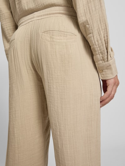 Męski model nosi Straight Fit Sweatpants in Musselin-Optik od Lindbergh, beżowa bawełna, muślinowa faktura, prosty krój, elastyczny pas z tunelem, szerokość w rozmiarze M: 41 cm, długość wewnętrzna nogawki: 81 cm, detaliczny kadr tylnej części.