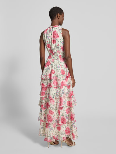 Frauenmodel trägt Maxikleid mit Schluppe Modell 'Marli' von Neo Noir aus Chiffon, florales Design in Rosa und Weiß, Volantsaum, Rückenansicht, Ganzkörperansicht Rückansicht, Taillierter Schnitt, Rückseitiger Schlüsselloch-Ausschnitt mit Knöpfen, Smok-Detail, Rückenlänge bei Größe 36: 145 cm, Brustweite bei Größe 36: 42 cm.