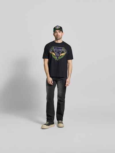 Männermodel trägt Regular Fit T-Shirt mit Logo-Print von RHUDE aus reiner Baumwolle, schwarz, Rundhalsausschnitt, Kurzärmelig, Ganzkörperansicht von vorne. Rückenlänge bei Größe M: 68 cm.