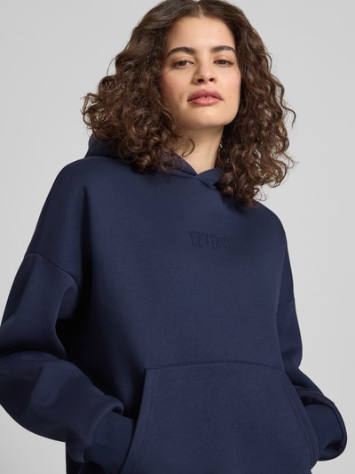 Modelka kobieca nosi Relaxed Fit Sweatshirt mit Logo-Print od Review z bawełnianej mieszanki, logo, kieszeń kangurka, elastyczne wykończenia, zbliżenie na górną część ciała