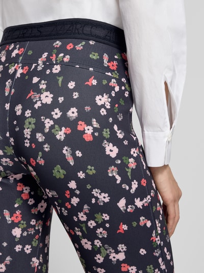 Männermodel trägt Flared Fit Leggins in verkürzter Passform von Marc Cain, elastyczna mieszanka materiałów, rozkloszowany krój, skrócony krój, elastyczny pas, szerokość w rozmiarze 36: 36 cm, długość wewnętrzna nogawki w rozmiarze 36: 69 cm, kwiatowy wzór na ciemnogranatowym tle, detailaufnahme