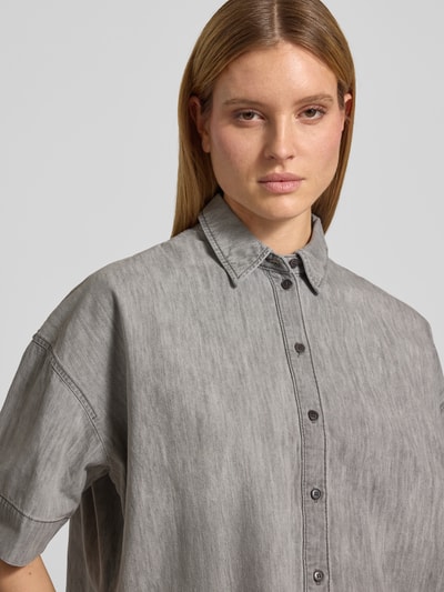 Kobiece modelka nosi bluzka jeansowa Boxy Fit z bawełny, model 'YARIKA' od Drykorn, kołnierzyk koszulowy, listwa guzikowa, szare odcienie, długość tyłu 53 cm, długość rękawów 22 cm, widok z przodu, zbliżenie na górną część ciała.