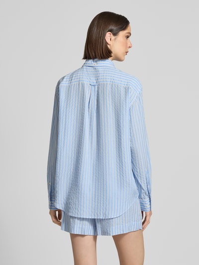 Frauenmodel trägt Relaxed Fit Bluse aus Lyocell mit Button-Down-Kragen von Gant in Blau mit weißen und gelben Streifen, Brusttasche und Knopfleiste, weiche Textur, Rückenlänge 73 cm, Ärmellänge 59 cm, Ganzkörperansicht Rückansicht.