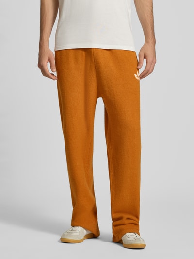 Männermodel trägt Wide Leg Weite Hose mit Woll-Anteil von adidas Originals in Orange, glatte Textur, Herren Weite Hose, Nahaufnahme Unterkörper