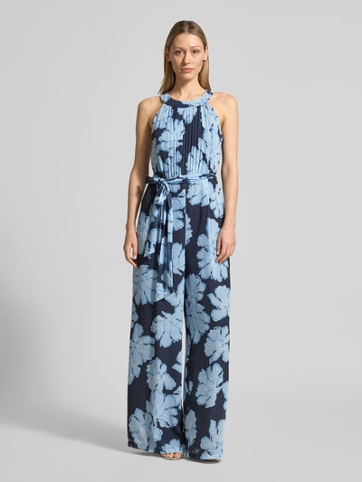 Modelka nosi Jumpsuit mit Bindegürtel und Plisseefalten von Christian Berg Cocktail, niebieski wzór kwiatowy, tkanina szyfonowa, krój slim fit, okrągły dekolt, pasek, długość całkowita 157 cm, szerokość w rozmiarze 36: 34 cm, całkowity widok z przodu.