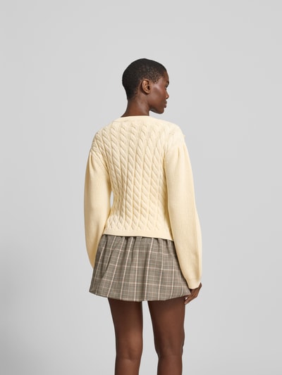 Frauenmodel trägt Strickjacke mit floralem Zierbesatz von BAUM & PFERDGARTEN aus reiner Baumwolle, taillierte Passform, Rückansicht, Rückenlänge 53 cm bei Größe S, Struktur durch Strickmuster, helle Farbe, strukturierte Oberfläche. Ganzkörperansicht Rückansicht.