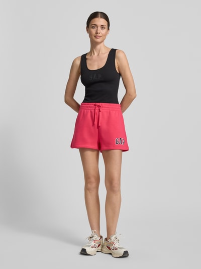 Frauenmodel trägt Sweatshorts mit Logo und elastischem Bund von GAP aus Baumwoll-Mix, Regular-Fit, pink mit weißem Logo, Ganzkörperansicht von vorne.