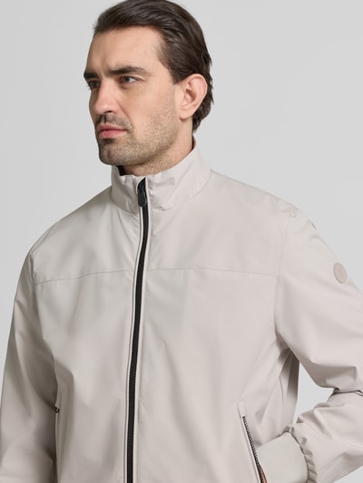 Männermodel trägt Regular Fit Jacke mit Stehkragen Modell 'Finlay' von SAVE THE DUCK in Beige mit Zweiwegereißverschluss, Nahaufnahme Oberkörper.