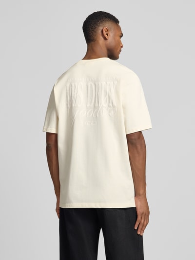 Männermodel trägt T-Shirt mit Label-Print Modell 'Ben Goods' von Les Deux in Offwhite, aus Bio-Baumwolle, Rückansicht, Ganzkörperansicht.