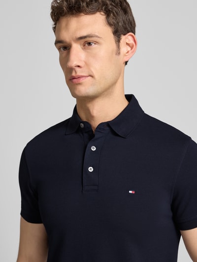 Männermodel trägt Slim Fit Poloshirt mit Stretch-Anteil van Tommy Hilfiger, donkerblauw, korte knoopsluiting, logo borduur, Nahaufnahme Oberkörper.
