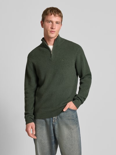 Männermodel trägt dunkelgrünen Strickpullover mit Stehkragen von Levi's®, reine Baumwolle, gerippte Abschlüsse, lockerer Schnitt, Ganzkörperansicht von vorne.