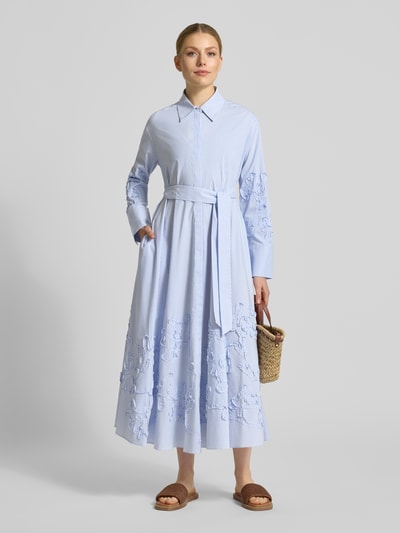 Frauenmodel trägt Hemdblusenkleid mit verdeckter Knopfleiste und Bindegürtel von Marc Cain, hellblauer Baumwoll-Mix, Midilänge, taillierter Schnitt, dezentes Streifenmuster, strukturierte Stickerei, Hemdblusenkragen, langärmlig, strukturierte Textur, Ganzkörperansicht von vorne.