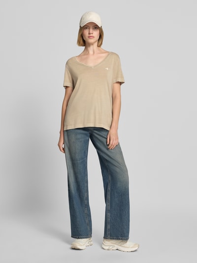 Frauenmodel trägt ein beiges Regular Fit T-Shirt aus Baumwoll-Mix von GANT, kombiniert mit blauer Jeans, Ganzkörperansicht von vorne.