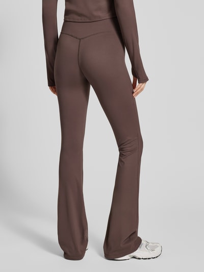 Frauenmodel trägt Flared Fit Leggings mit breitem Bund Modell 'Yoga' von Gina Tricot in Braun, elastischer Material-Mix, Ganzkörperansicht Rückansicht.