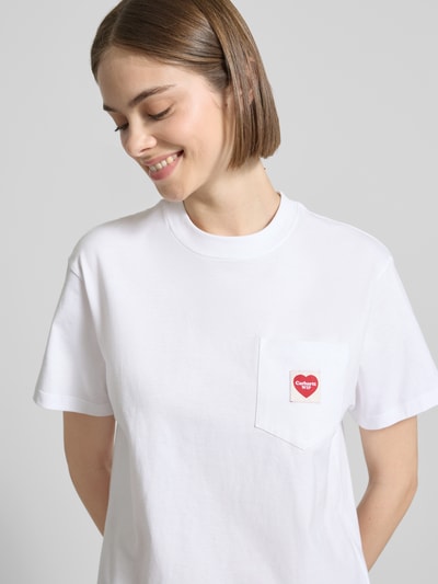 Frauenmodel trägt Damen T-Shirt mit Label-Patch von Carhartt Work In Progress in Weiß, Reine Baumwolle, Gerader-Schnitt, Rundhalsausschnitt, Brusttasche, Rückenlänge bei Größe S 58 cm, Nahaufnahme Oberkörper.