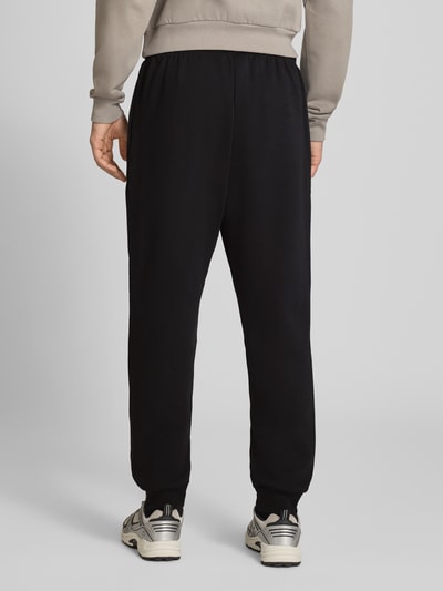 Männermodel trägt Relaxed Fit Sweatpants aus Mieszanka bawełny Modell 'EVOLUTION' von The North Face w kolorze czarnym, wpuszczane kieszenie, tunel w pasie, długość wewnętrzna nogawki 75 cm w rozmiarze M, Ganzkörperansicht Rückansicht.