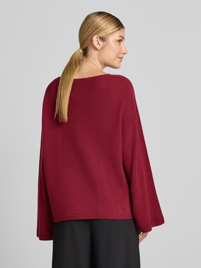 Frauenmodel trägt Oversized Pullover aus reiner Baumwolle in Strick-Optik von Emporio Armani in Dunkelrot mit elastischen Abschlüssen, Ganzkörperansicht Rückansicht.