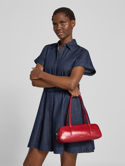 Frauenmodel trägt dunkelblaue Hemdblusenkleid und Henkeltasche mit Label-Prägung Modell 'FOIL LOGO GLOSSY BAULETTO' von CK Calvin Klein, rote glänzende Oberfläche, Damen Henkeltasche von CK Calvin Klein, Nahaufnahme Oberkörper.