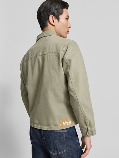 Männermodel trägt Jeansjacke mit Reißverschluss Modell 'REILLY' von khujo in hellem Oliv, Reine Baumwolle, Gerader-Schnitt, Ganzkörperansicht Rückansicht.