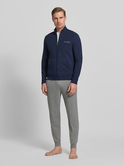 Männermodel trägt Sweatjacke mit Logo und Stehkragen von JOOP! Collection, Baumwoll-Elasthan-Mix, Regular-Fit, Ganzkörperansicht von vorne.