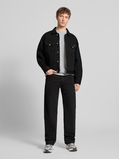 Męski model nosi Jeansjacke mit Brusttaschen und Label-Detail od Calvin Klein Jeans, czarna bawełna, krój regular fit, widok całej sylwetki z przodu.
