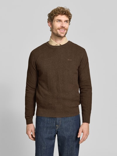 Männermodel trägt Regular Fit Pullover aus Baumwoll-Woll-Mix von GANT in Braun mit feiner Struktur, blaue Jeans, Ganzkörperansicht von vorne.