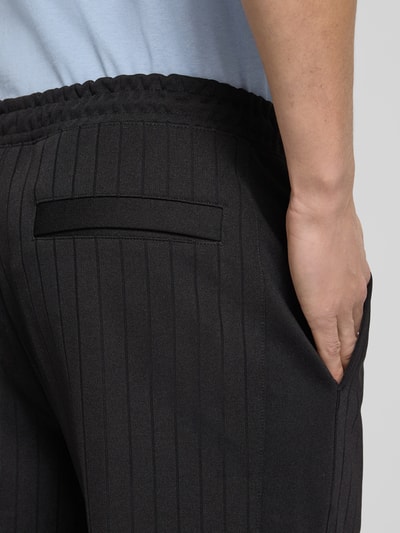 Männermodel trägt Regular Fit Sweatpants aus Baumwoll-Mix Modell 'DAVROPANT' von HUGO in Schwarz mit Streifenmuster, Nahaufnahme Hüfte.