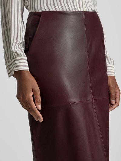 Frauenmodel trägt Lederrock aus echtem Leder in Midilänge von windsor., dunkelbraune Farbe, glatte Textur, Nahaufnahme Oberkörper.