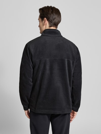 Männermodel trägt Fleecepullover mit Stehkragen und Label-Detail von Columbia in Schwarz, Regular-Fit, Ganzkörperansicht Rückansicht. Rückenlänge 70 cm, Ärmellänge 66 cm, Modell STEENS MOUNTAIN, Knopfleiste.