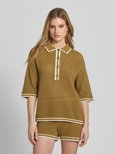 Frauenmodel trägt Strickshirt mit Polokragen und Knopfleiste von Style Icon Collection, reine Baumwolle, grob gestrickt, senfgelb mit weißen Kontraststreifen, überschnittene Schultern, gerader Schnitt, 3/4-Arm, Ganzkörperansicht von vorne.