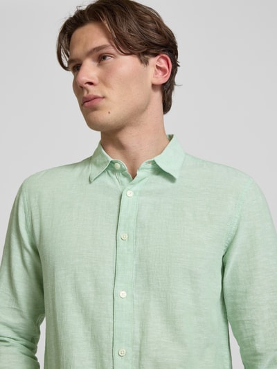 Mannenmodel draagt Slim Fit Freizeithemd aus Baumwoll-Leinen-Mix Modell 'CAIDENLS SOLID' van Only & Sons, effen lichtgroen met kentkraag, slanke pasvorm, lange mouw, zichtbare knoopsluiting, licht gestructureerde katoen-linnenmix, detailopname bovenlichaam.