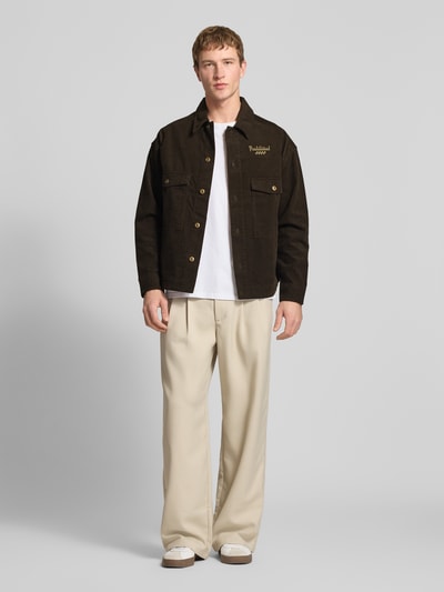 Männermodel trägt Regular Fit Hemdjacke aus reiner Baumwolle Modell 'Pitstop' von PROHIBITED in Cord mit Umlegekragen, durchgehender Knopfleiste, Brusttaschen und Label-Applikation in metallic, Rückenlänge 70 cm, Schulterbreite 59 cm, Ärmellänge 59 cm; neutrale Farben, klare Struktur, Ganzkörperansicht von vorne.