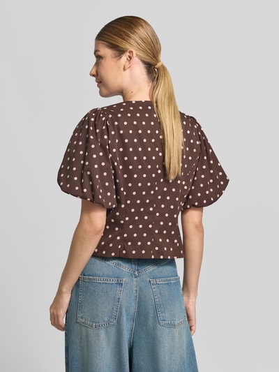 Vrouwenmodel draagt blouse met korte mouwen Model 'ANELA' van Neo Noir, bruin met beige stippen, ballonmouwen, nauwsluitend, ruglengte maat 36: 48 cm, mouwlengte: 28 cm, ronde hals, doorlopende haakjessluiting, volledige lichaamsweergave achteraan.