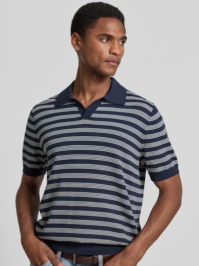 Mężczyzna nosi Regular Fit Poloshirt mit V-Ausschnitt od Christian Berg Men, bawełna, kołnierzyk polo, dekolt w serek, krój regular fit, długość tyłu w rozmiarze M 68 cm, długość rękawów w rozmiarze M 27 cm, granatowe i białe paski, widok z przodu, zbliżenie na górną część ciała.