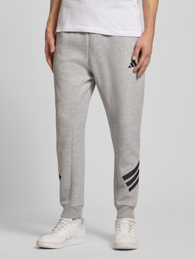 Männermodel trägt Slim Fit Sweathose mit Logo-Print von adidas Sportswear, grau, Baumwoll-Mix, elastischer Bund, Ganzkörperansicht von vorne.