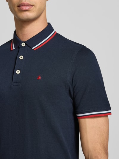 Männermodel trägt Slim Fit Poloshirt mit Viskose-Anteil Modell 'Paulos' von JACK & JONES, Baumwoll-Mix, Logo-Stitching, Nahaufnahme Oberkörper.