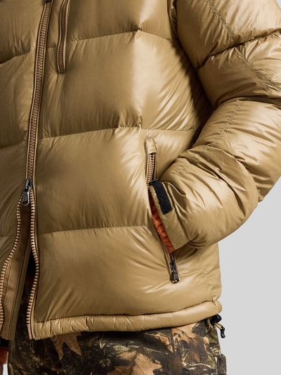 Männermodel trägt Regular Fit Steppjacke mit Zweiwege-Reißverschluss von Polo Ralph Lauren in Beige mit glatter Struktur, Nahaufnahme Oberkörper.