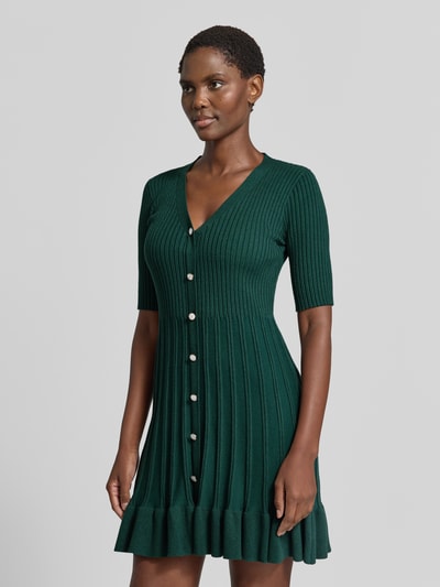 Frauenmodel trägt Strickkleid in Minilänge mit Viskose-Anteil von Christian Berg Woman, grün, Ripp-Optik, Knopfleiste, Ganzkörperansicht von vorne.