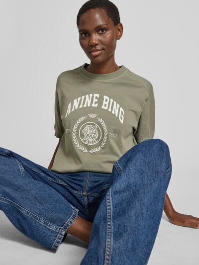 Frauenmodel trägt Oversized Sweatshirt mit Logo-Detail von Anine Bing in Olivgrün aus reiner Baumwolle mit Rundhalsausschnitt, elastischen Abschlüssen, oversized Fit, Rückenlänge 62 cm bei Größe S, Ganzkörperansicht von vorne.