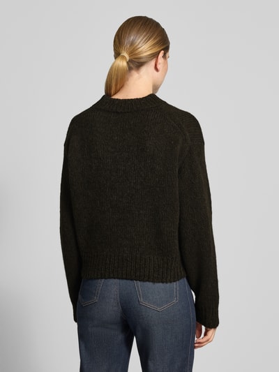 Frauenmodel trägt Relaxed Fit Strickpullover aus Woll-Alpaka-Mix von Marc Cain in Dunkelgrün, grobe Textur, Ganzkörperansicht Rückansicht. Damen Pullover, Lanawoll-Mix mit Alpaka-Anteil, gerippte Abschlüsse, überschnittene Schultern, langärmlig, Rundhalsausschnitt, Rückenlänge bei Größe 36: 51 cm, Ärmellänge: 62 cm.