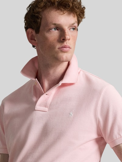 Männermodel trägt Regular Fit Poloshirt aus reiner Baumwolle von Polo Ralph Lauren in effen lichtroze piqué, logo-detail, polokraag, V-hals, korte knopenlijst, korte mouw met geribd uiteinde, zoom met zijsplitten en asymmetrisch, close-up bovenlichaam.