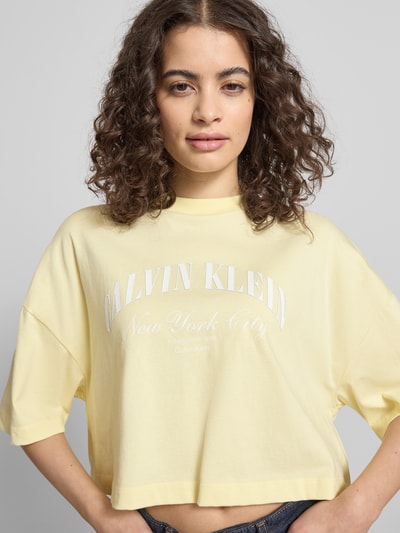 Frauenmodel trägt Cropped T-Shirt mit Logo-Print von Calvin Klein Jeans in Gelb, reine Baumwolle, Rundhalsausschnitt, Nahaufnahme Oberkörper.
