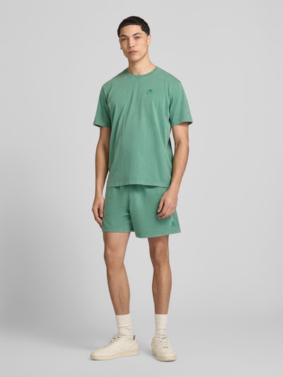 Männermodel trägt grüne Sweatshorts mit Eingrifftaschen von CHAMPION aus Baumwoll-Mix, Regular Fit, ganzkörperansicht von vorne.