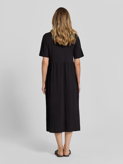 Frauenmodel trägt schwarzes Damen Midikleid mit Smok-Details Modell 'DERBY' von Soyaconcept aus reiner Baumwolle, A-Linie, Rundhalsausschnitt, Rückenlänge 117 cm, Brustweite 44 cm, Ärmellänge 27 cm, Ganzkörperansicht Rückansicht.
