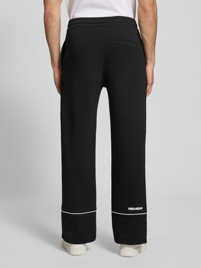 Mężczyznęmodel nosi Sweatpants mit elastischem Bund und Logo od REVIEW, bawełna, krój relaxed fit, czarne, logo, długość wewnętrzna nogawki 78 cm, widok całej sylwetki z tyłu.
