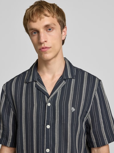Männermodel trägt Relaxed Fit Freizeithemd mit Logo-Stitching von REVIEW in Dunkelblau mit Streifen, Reverskragen, Nahaufnahme Oberkörper.
