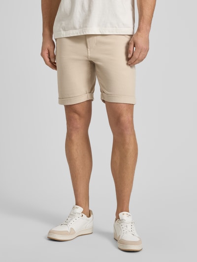 Męski model nosi Slim Fit Chinoshorts aus Baumwoll-Mix Modell 'SLIM-LUTON' od SELECTED HOMME, jednokolorowy beż, krój slim fit, mieszanka bawełny, wpuszczane kieszenie, aplikacja z metką, tkana faktura, zapięcie na guzik i ukryty zamek, widok z przodu na całe ciało.