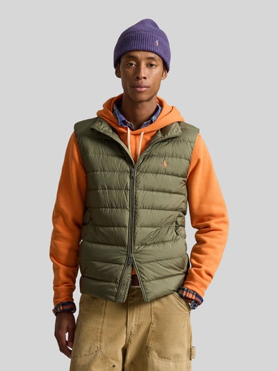 Männermodel trägt Regular Fit Weste mit Logo-Stitching von Polo Ralph Lauren in Olivgrün, kombiniert mit oranger Kapuzenjacke, Ganzkörperansicht von vorne.
