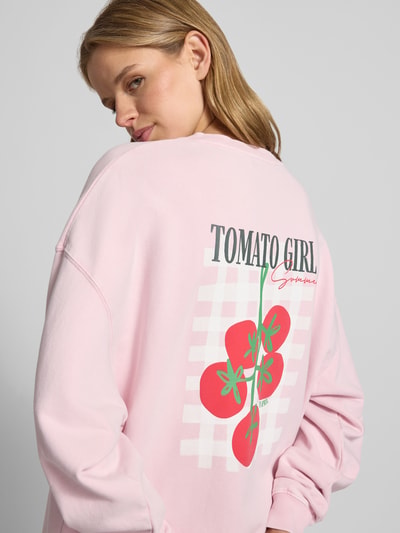 Frauenmodel trägt Oversized Sweatshirt mit rückseitigem Statement-Print von OH APRIL in Rosa mit rotem und grünen Print, Ganzkörperansicht Rückansicht.